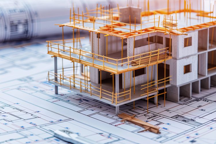 a detailed architectural model of a multi-story building under construction, placed on top of technical blueprints